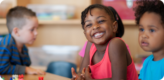 photo of child smiling in early learning center setting with two other children