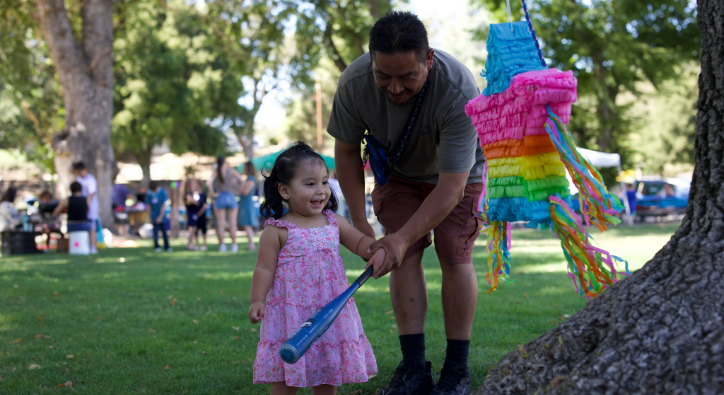 image of young child with adult holding a bat getting ready to hit the pinata. 